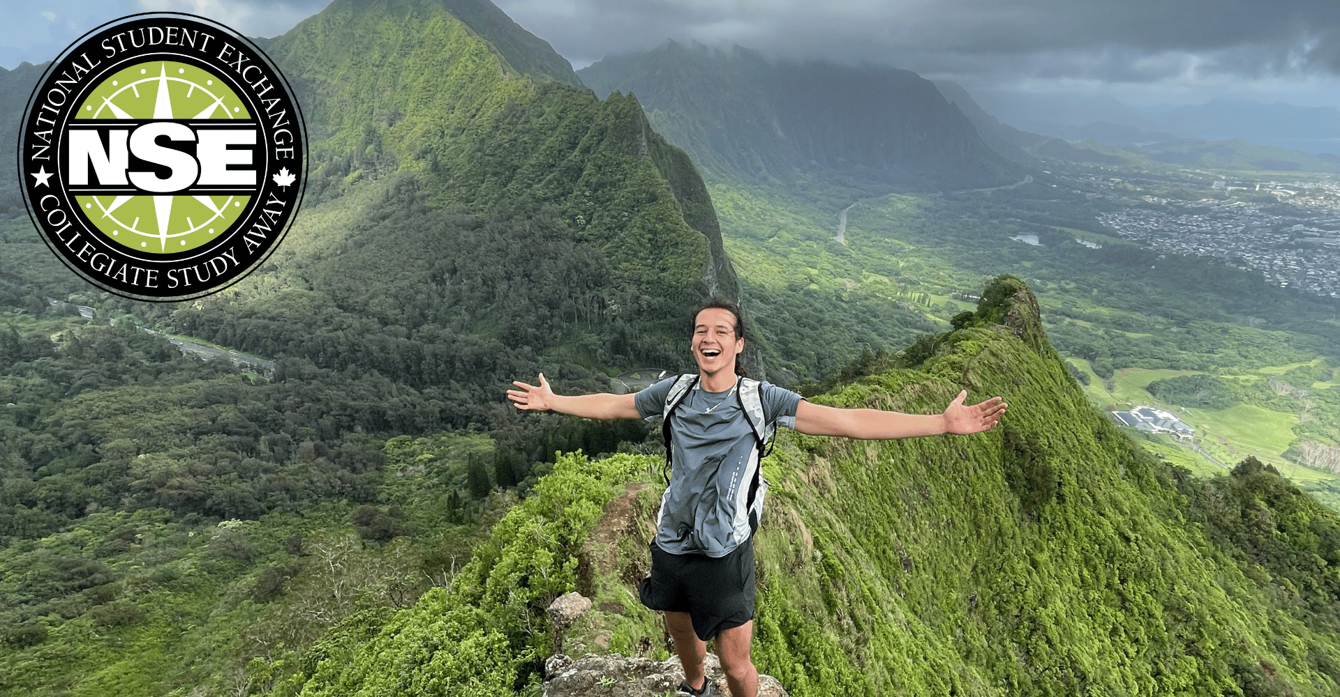 Student hiking in hawaii at the top arms outstretched with nse logo