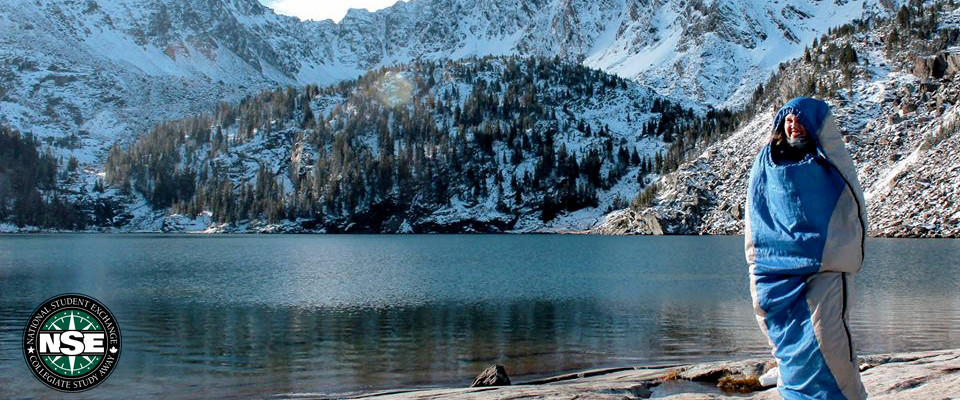 NSE student stands by a lake surrounded by snow covered mountains